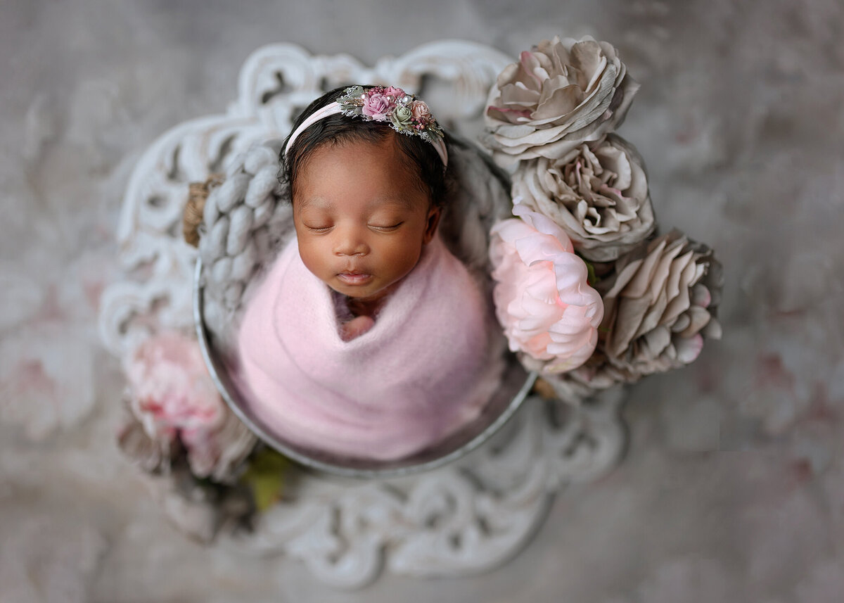 beautiful baby girl swaddled in pink wrap in a bucket with pink and gray flowers on a floral background