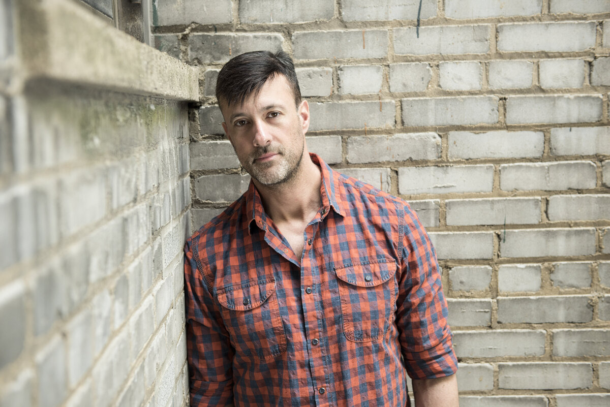 A person in a plaid shirt leaning against a bright building