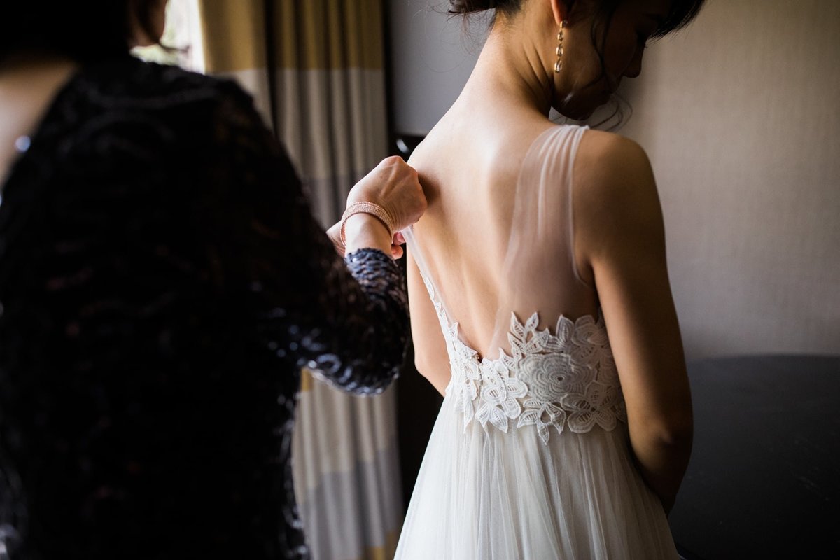 Mother of the Bride adjusts the back of the Bride's dress while getting ready