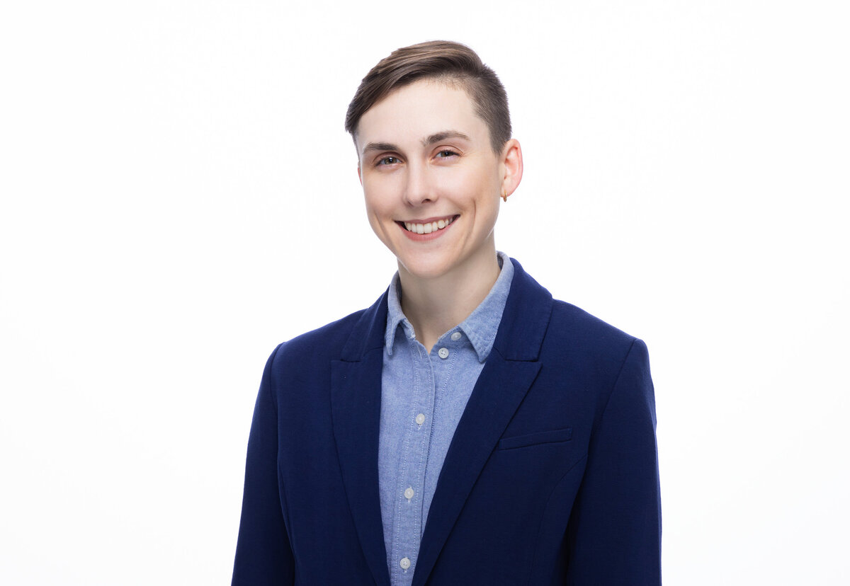 Capture the professional essence of Cincinnati with this high-resolution portrait of an individual named Jules Madzia. Their confident and welcoming smile complements the sharp attire, consisting of a navy blue blazer over a light blue shirt, adding a touch of sophistication ideal for personal branding. Noteworthy for its clear and vibrant quality, this portrait, set against a flawless white background, showcases the subject's short hairstyle and the subtle sheen of their earrings. It embodies the spirit of Cincinnati's professional scene, making it a perfect representation for a modern headshot.