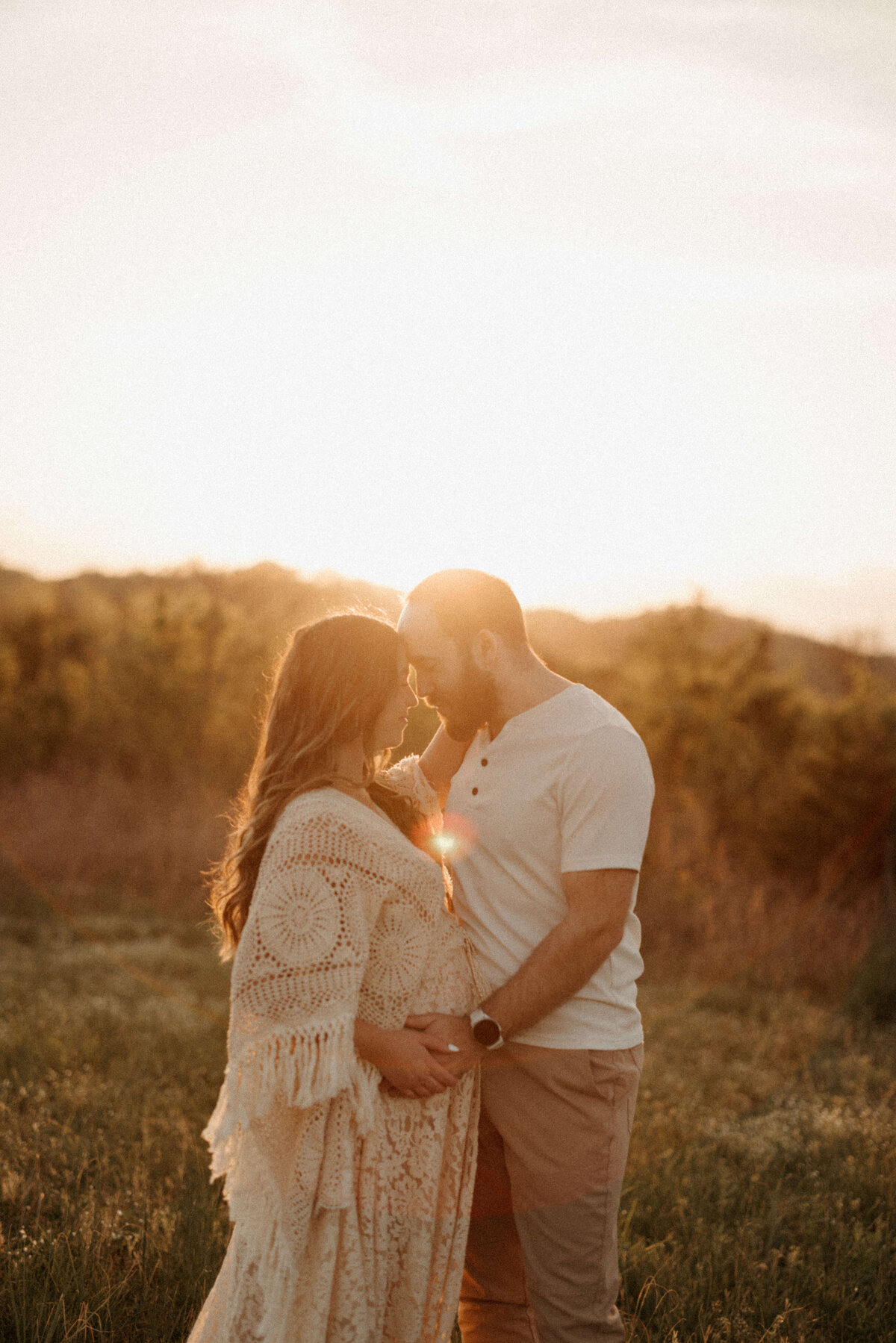 Maternity photo of woman in white dress standing in tall grass at golden hour in franklin TN