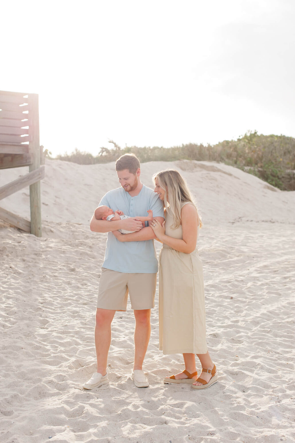 Parents stand on the beach in beautiful neutrals and blues holding their new baby boy
