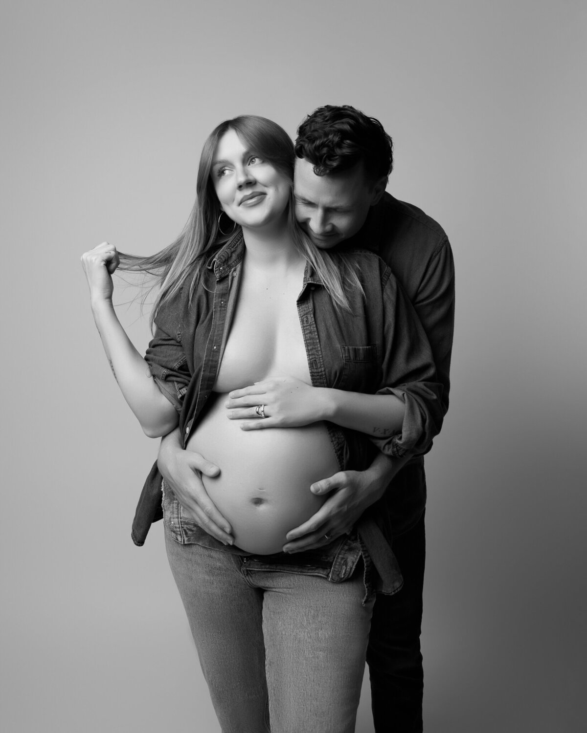 Playful maternity photo of a couple in denim posing in studio near Leander, TX