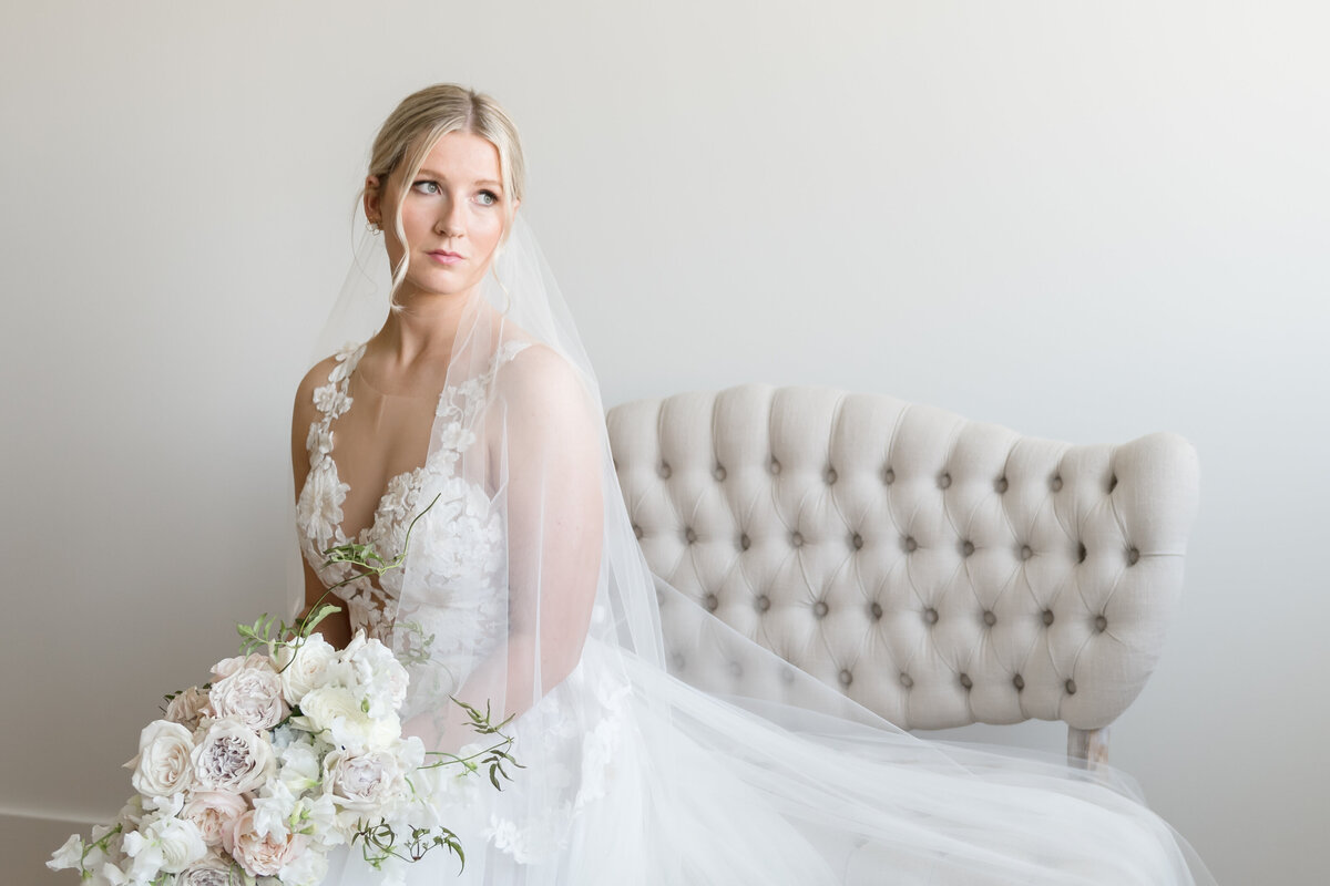 bride sitting on bench looking towards window with bouquet in lap