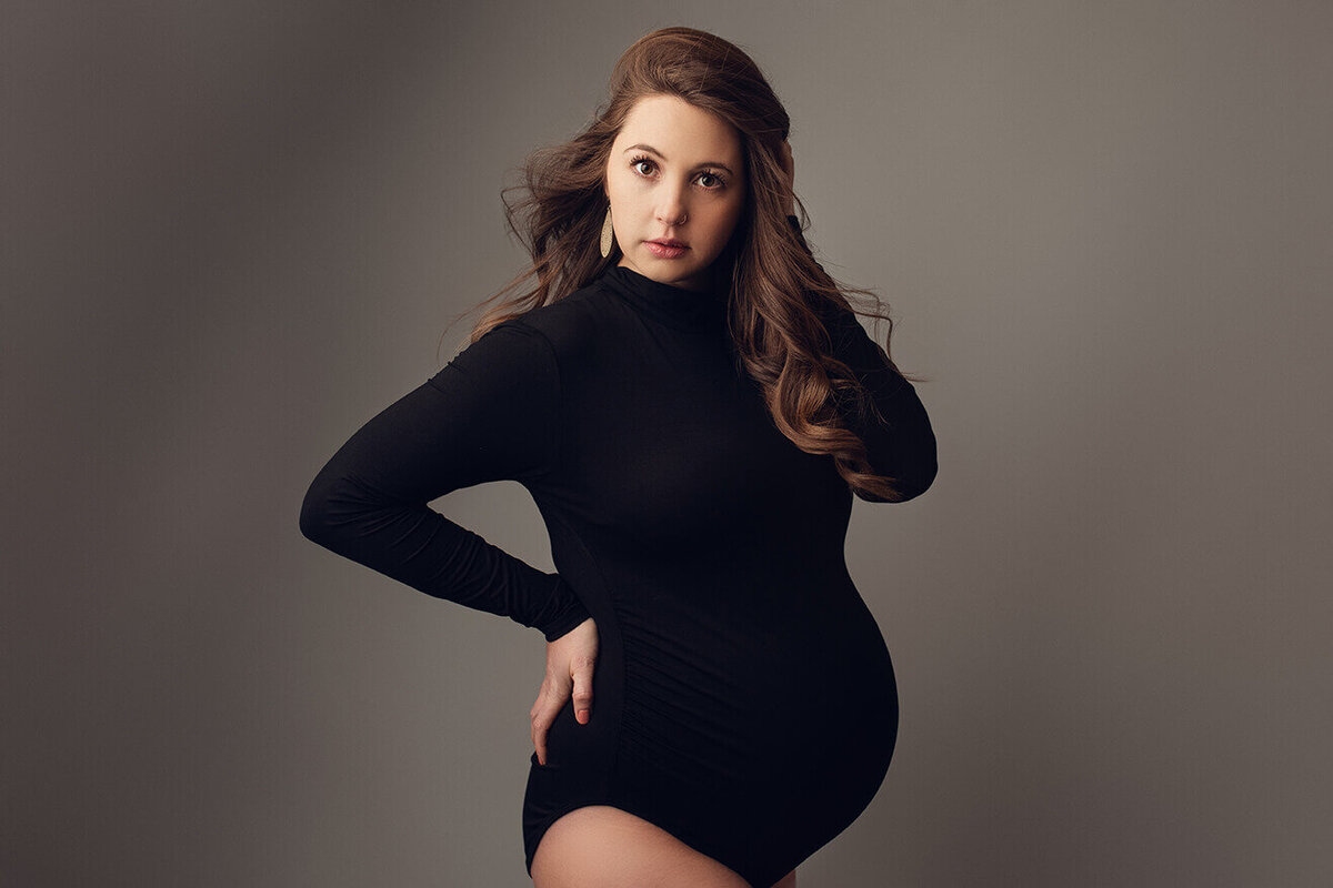 Pregnant woman wearing a black body suit holding her hair