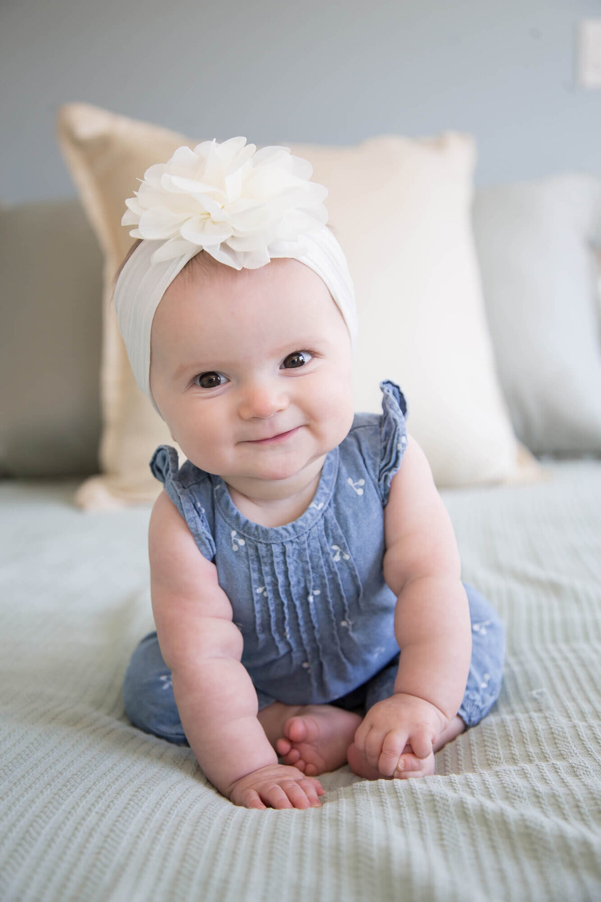 adorable baby girl in denim romper sitting on a bed