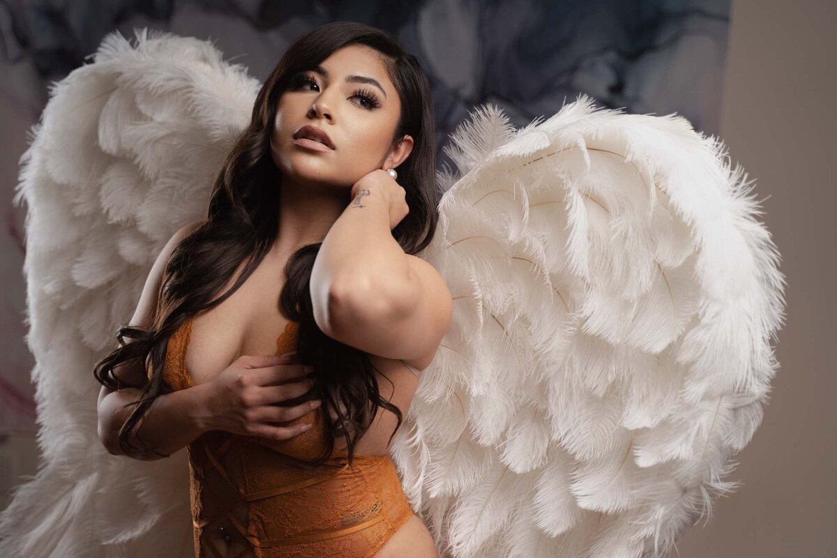Asian woman posing in luxurious boudoir portrait featuring white wings prop