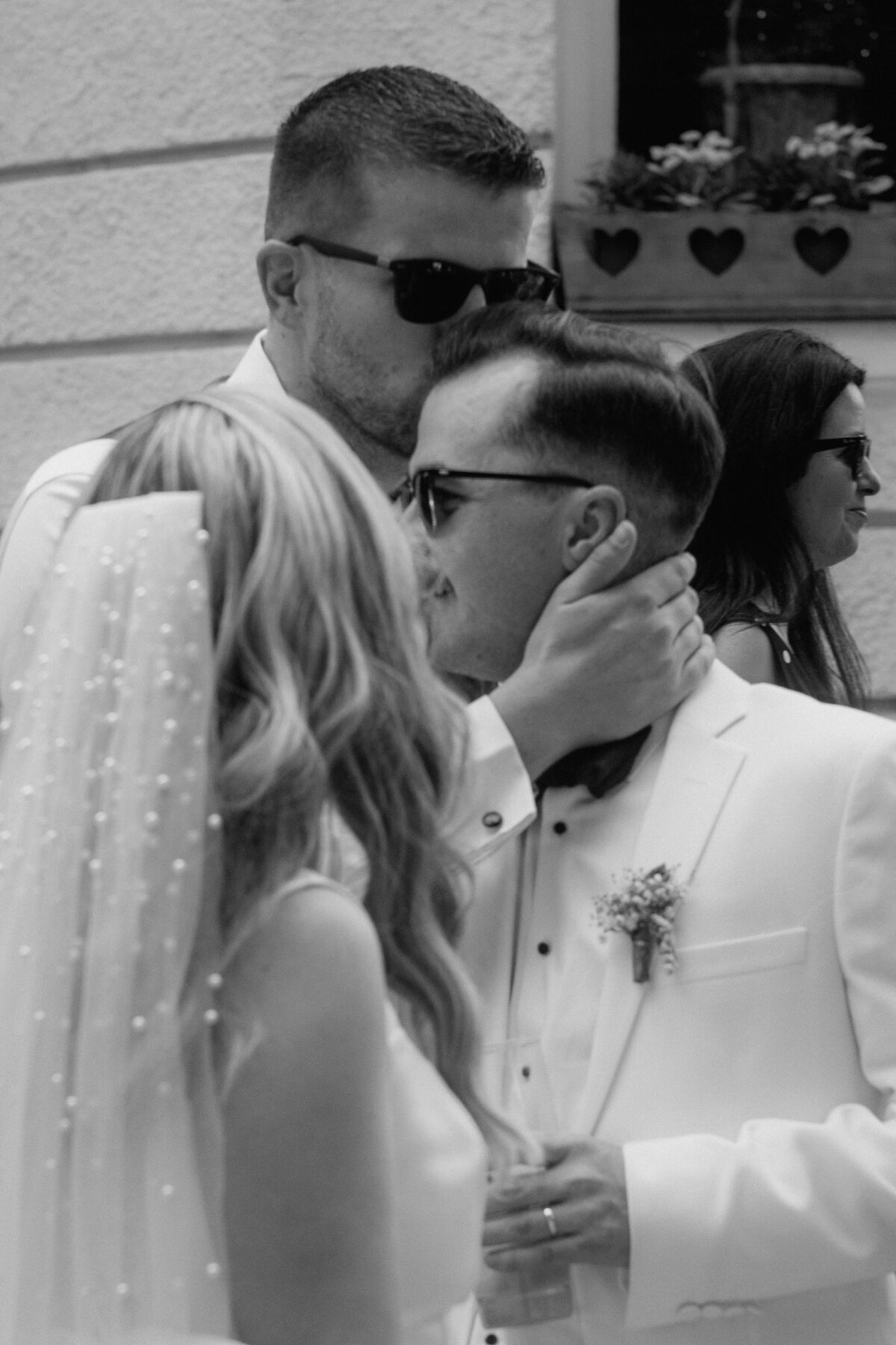 Der Bräutigam wird von einem männlichen Gast mit Sonnenbrille auf den Kopf geküsst.