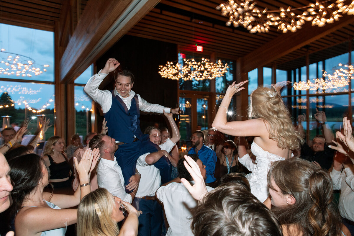 Colorful image of bride and groom being held on their friends shoulders on the dance floor at their wedding.