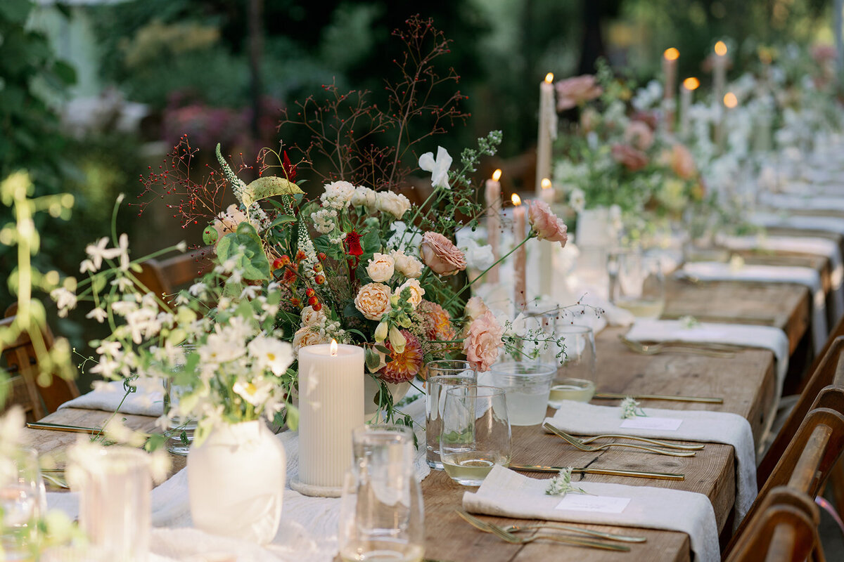 Elegant long family-style reception table inside Glasshouse Community greenhouse with candles and floral centerpieces for a summer wedding.