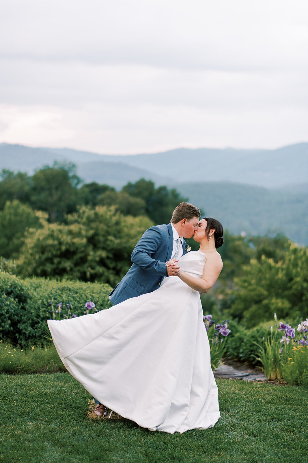 Bride and groom kissing at sunset with mountain views during their elegant Cashiers NC wedding.
