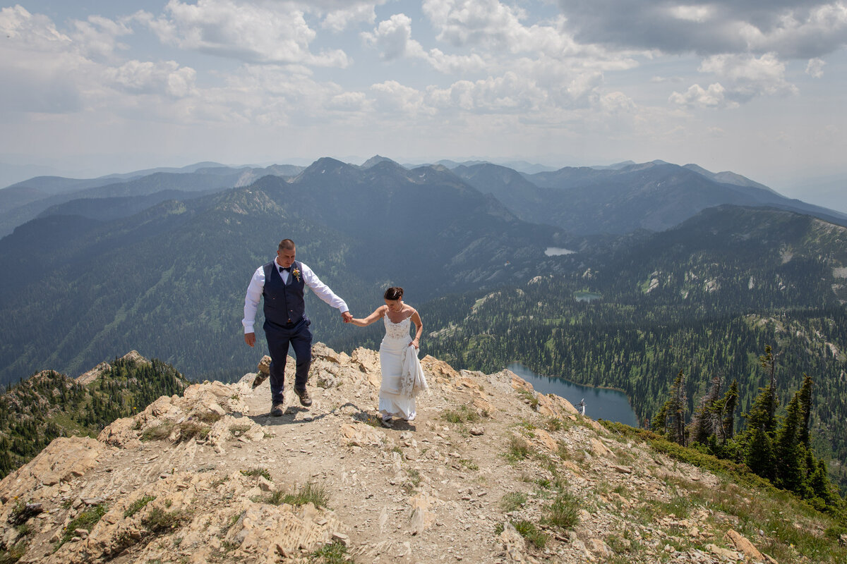 A bride and groom walk hand in hand up a hillside as their Montana elopement photographers take their photos.