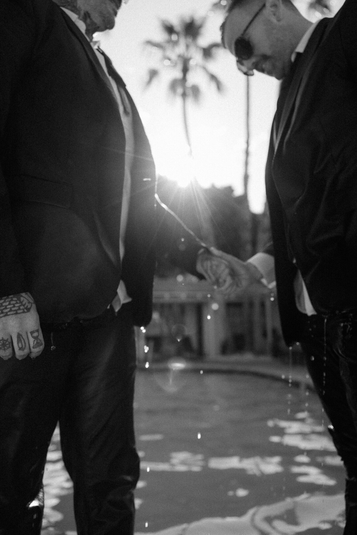Grooms hold hands in old Hollywood style classic black and white photo near pool at Villa Royal. 