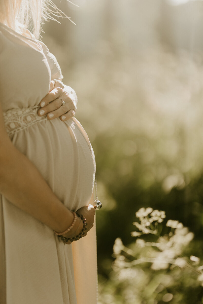 Profil de femme enceinte entourant son ventre de ses mains dans un décor verdoyant. Photo prise par Laura, photographe grossesse en Vendée.