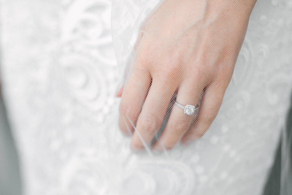 Bride engagement ring under veil  white lace wedding dress showing