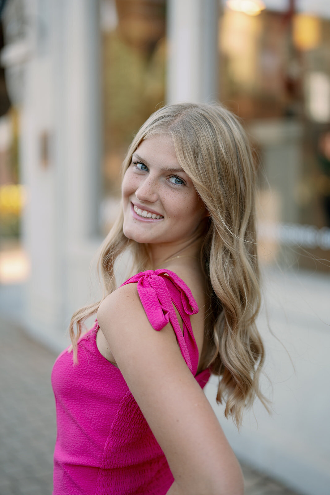 Senior girl standing and smiling with the streets of downtown Holland blurred behind her during her senior photos.