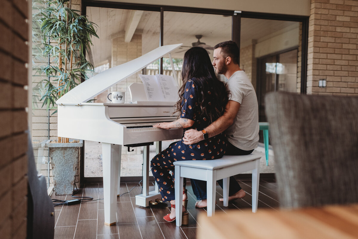 Couples Photography, man embraces woman as she plays grand piano in the living room