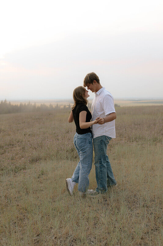 Facing each other, a couple hold hands with their noses almost touching. They're standing in a field in Rexburg, Idaho.