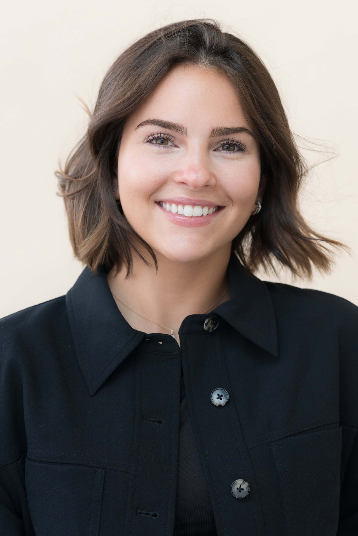 Close-up headshot of a beautiful woman with dark hair smiling while posing in a dark suit