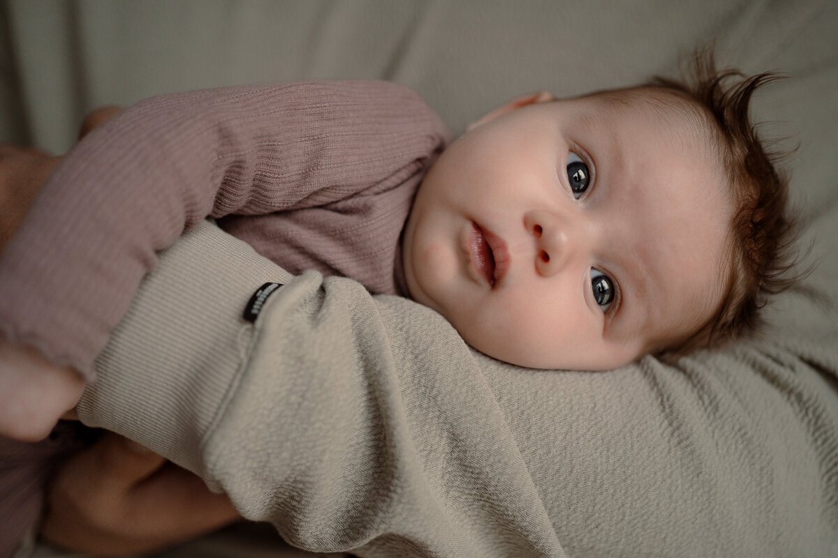 Closup van newborn die in de armen van papa ligt en met open ogen kijkt tijdens een newbornshoot