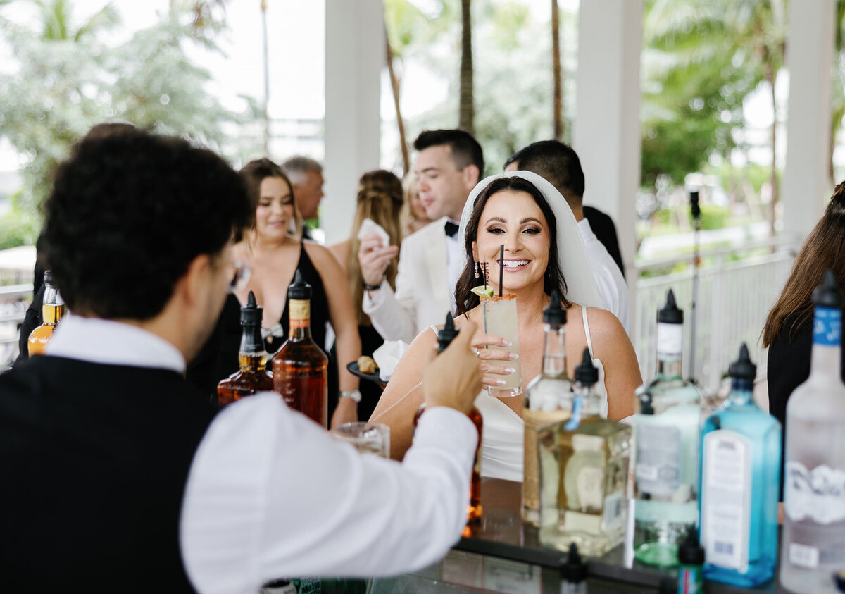 The bride smiling with her cocktail in hand, enjoying a celebratory moment at Ashley and Cameron's micro wedding at Ocean Reef in Key Largo, captured by Claudia Amalia Photography.