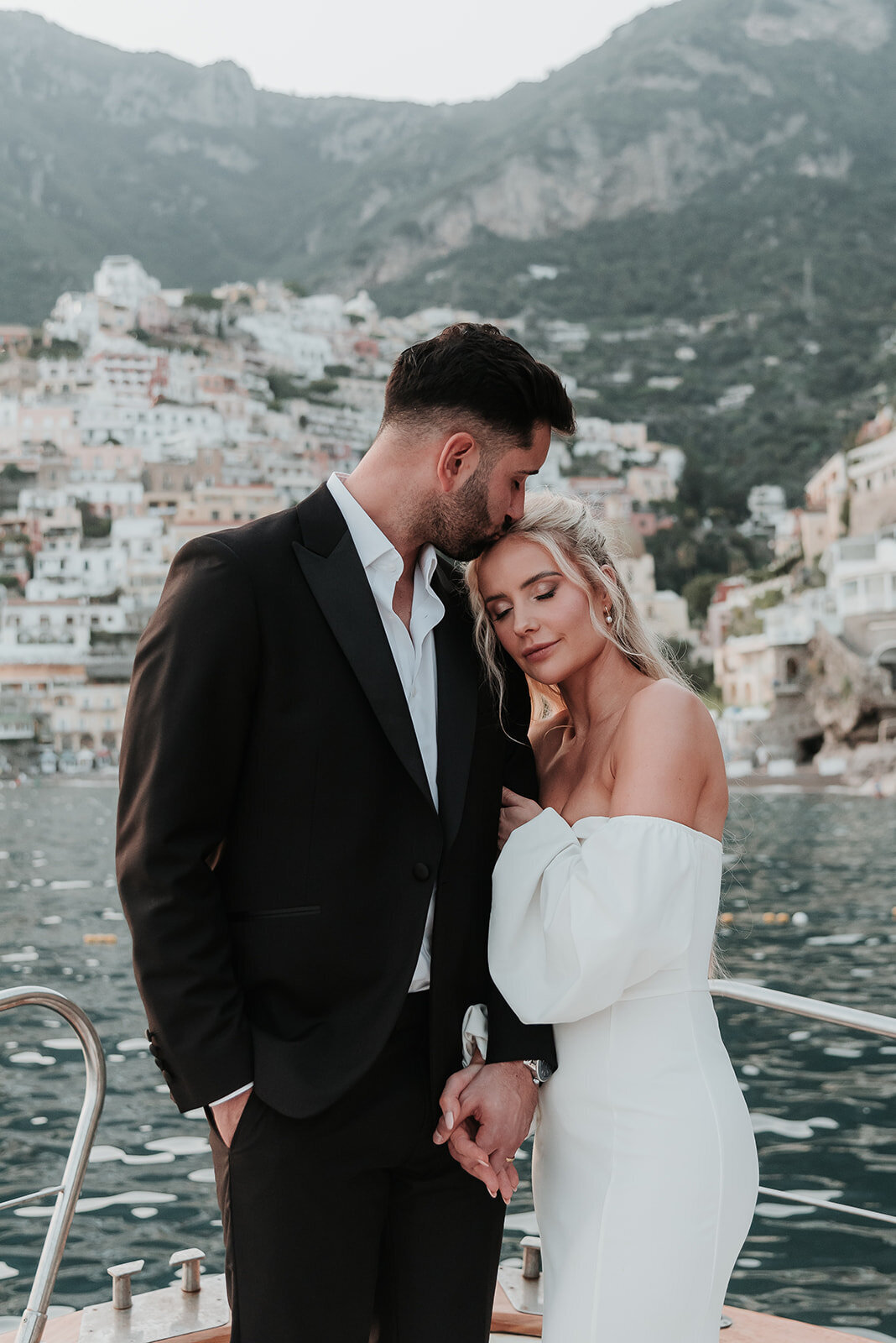 Brida and Groom lean in closely to one another enjoying a boat ride on the island of Positano