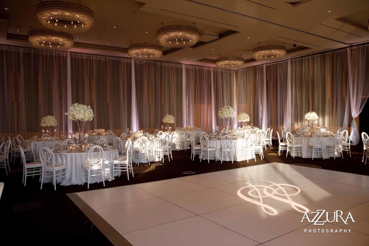 all white wedding with white dance floor, white wall draping, and a gobo light on dance floor