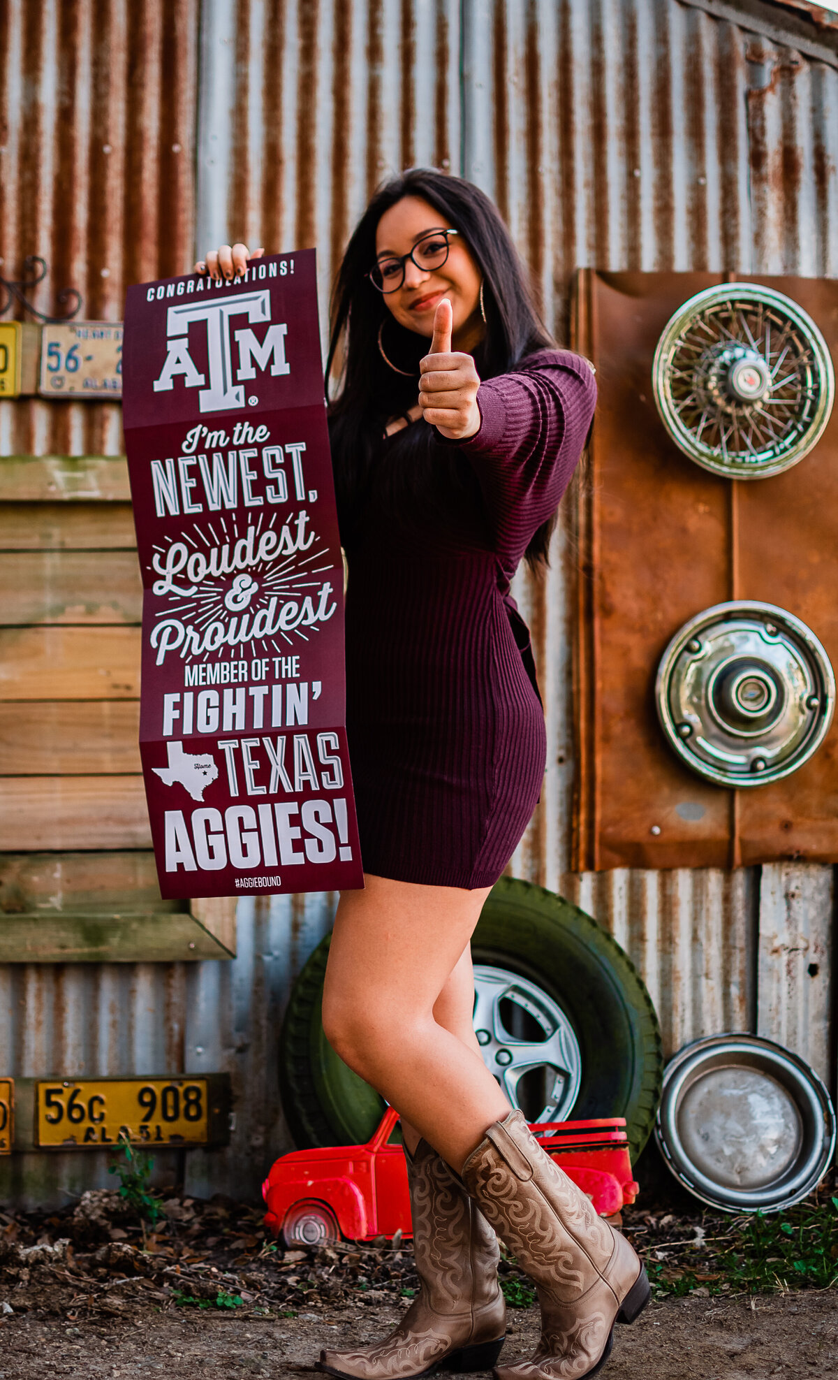 A recent graduate hold a Texas A&M  banner while showing the "gig em" sign.