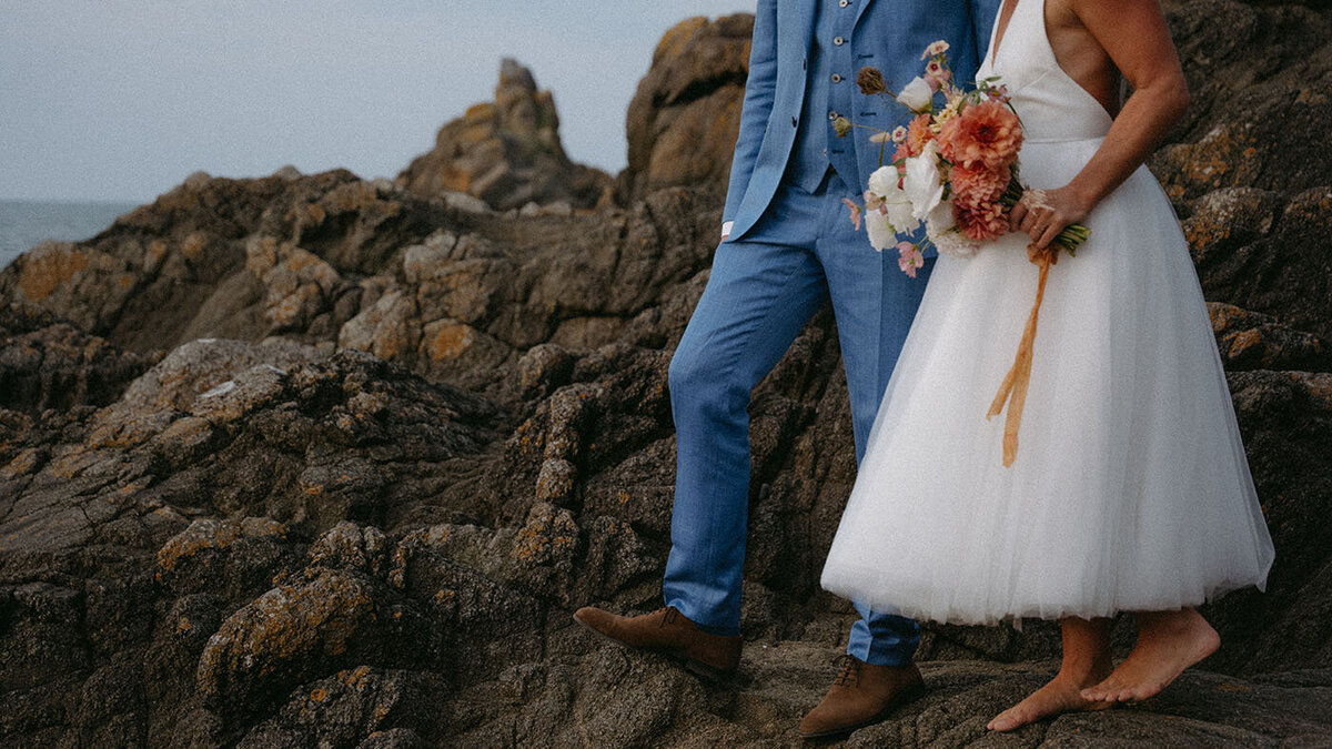 Mariés avançant pieds nus sur les rochers en bord de mer. Image poétique réalisée par Kamescop, vidéaste et photographe mariage en Bretagne.