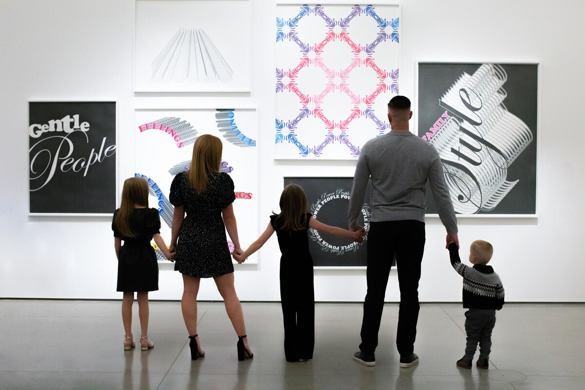 A family of five holding hands while looking at a wall of art with their backs to the camera at Orange County Museum of Art.