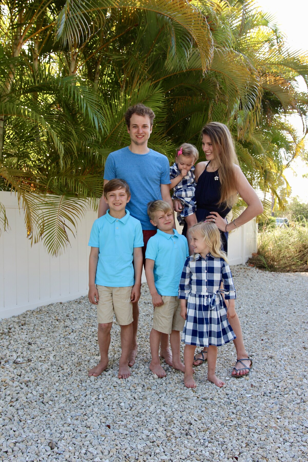 Family smiles for a photo at the beach with sun rays and palm trees