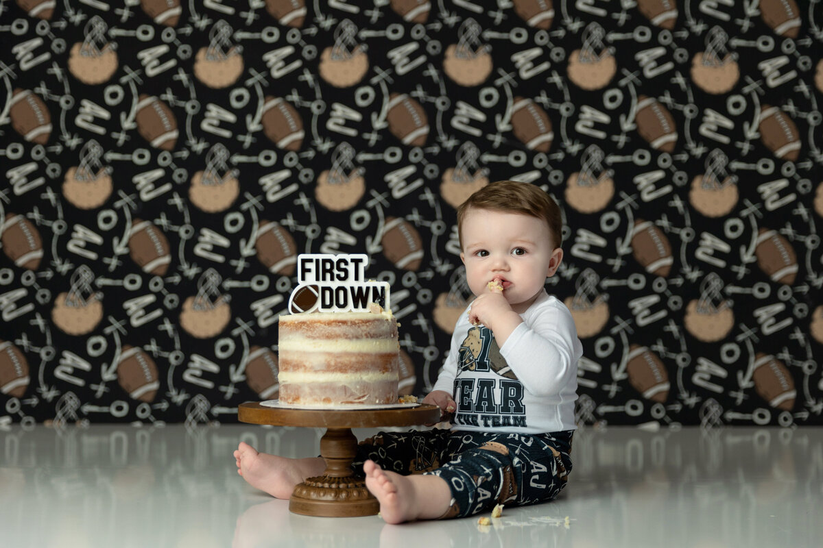 A toddler boy in a football outfit for his first birthday tastes a cake