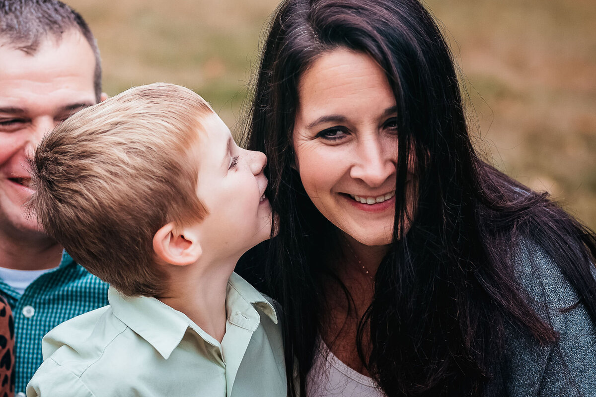 Little boy whispering in mothers ear at family photo session at Stark Park in Manchester NH by Lisa Smith Photography