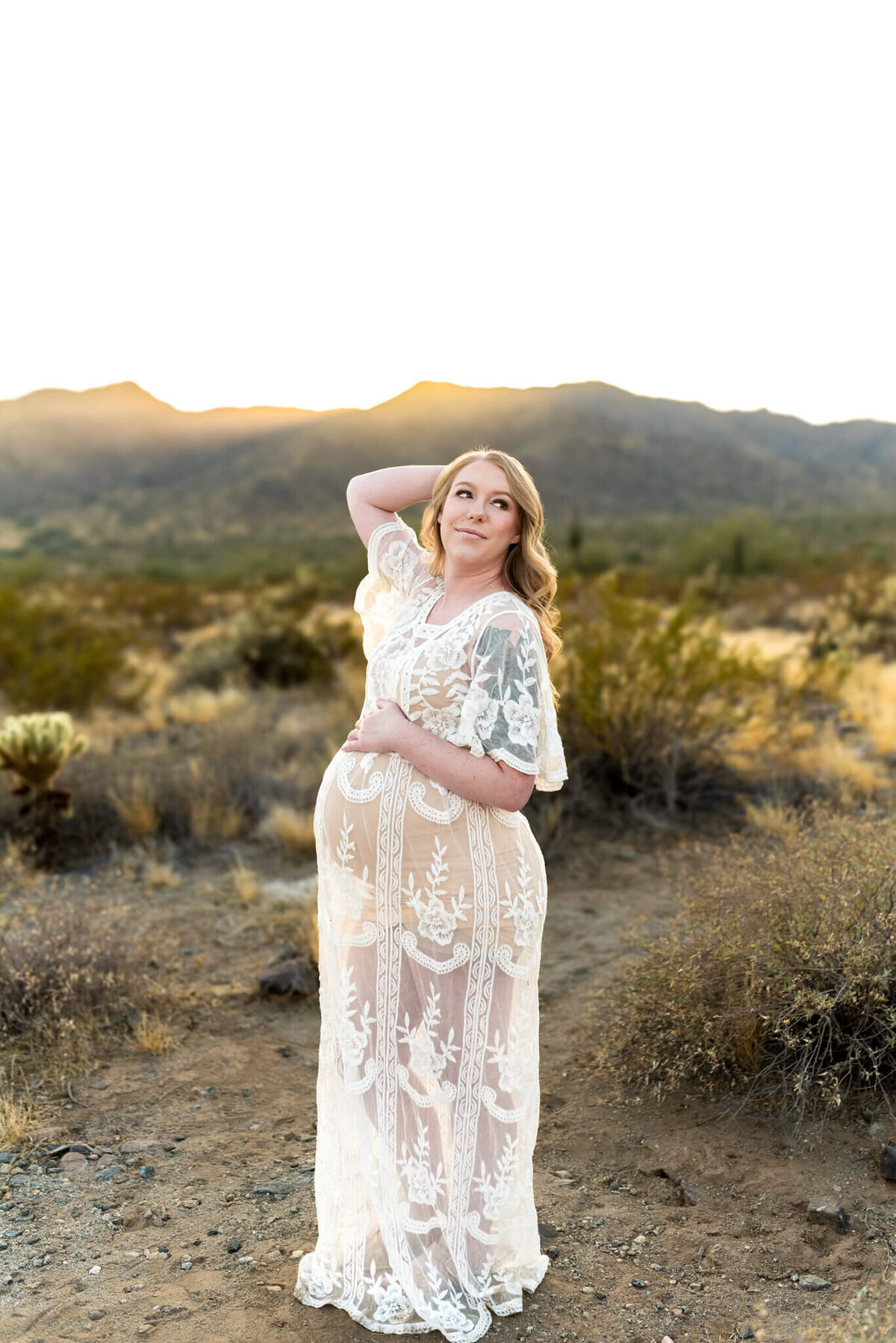 mom wearing white lace dress posing in the sunset light for pregnancy photo