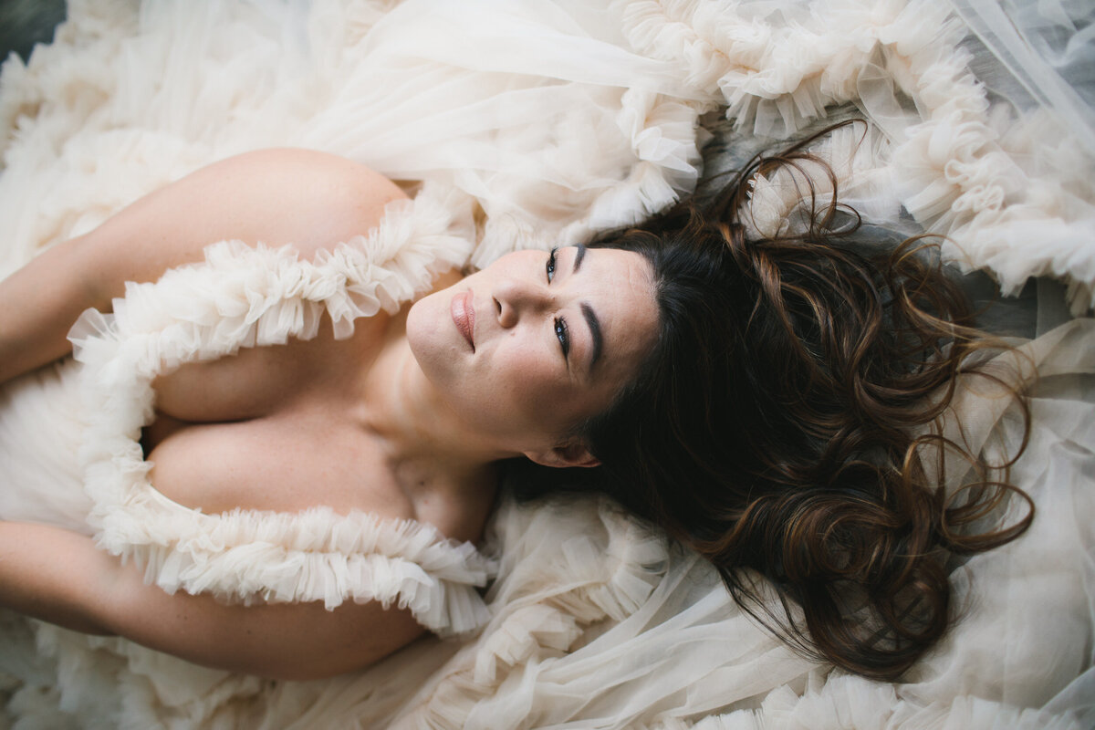 Curvy woman in white tulle robe smiling posed on the floor