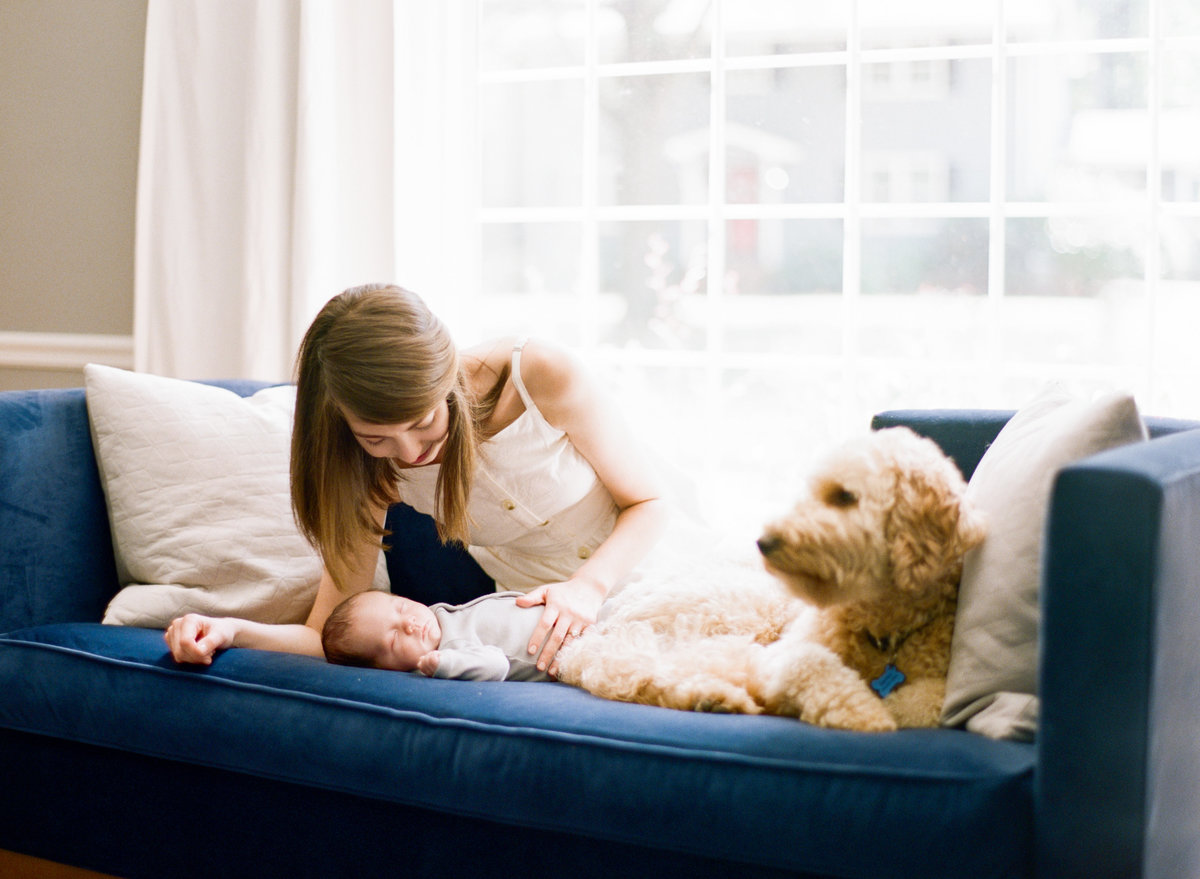 Mom and dog lay on a couch snuggling their new baby during their lifestyle newborn photography session in Raleigh NC. Photographed by Raleigh Newborn Photographer A.J. Dunlap Photography.