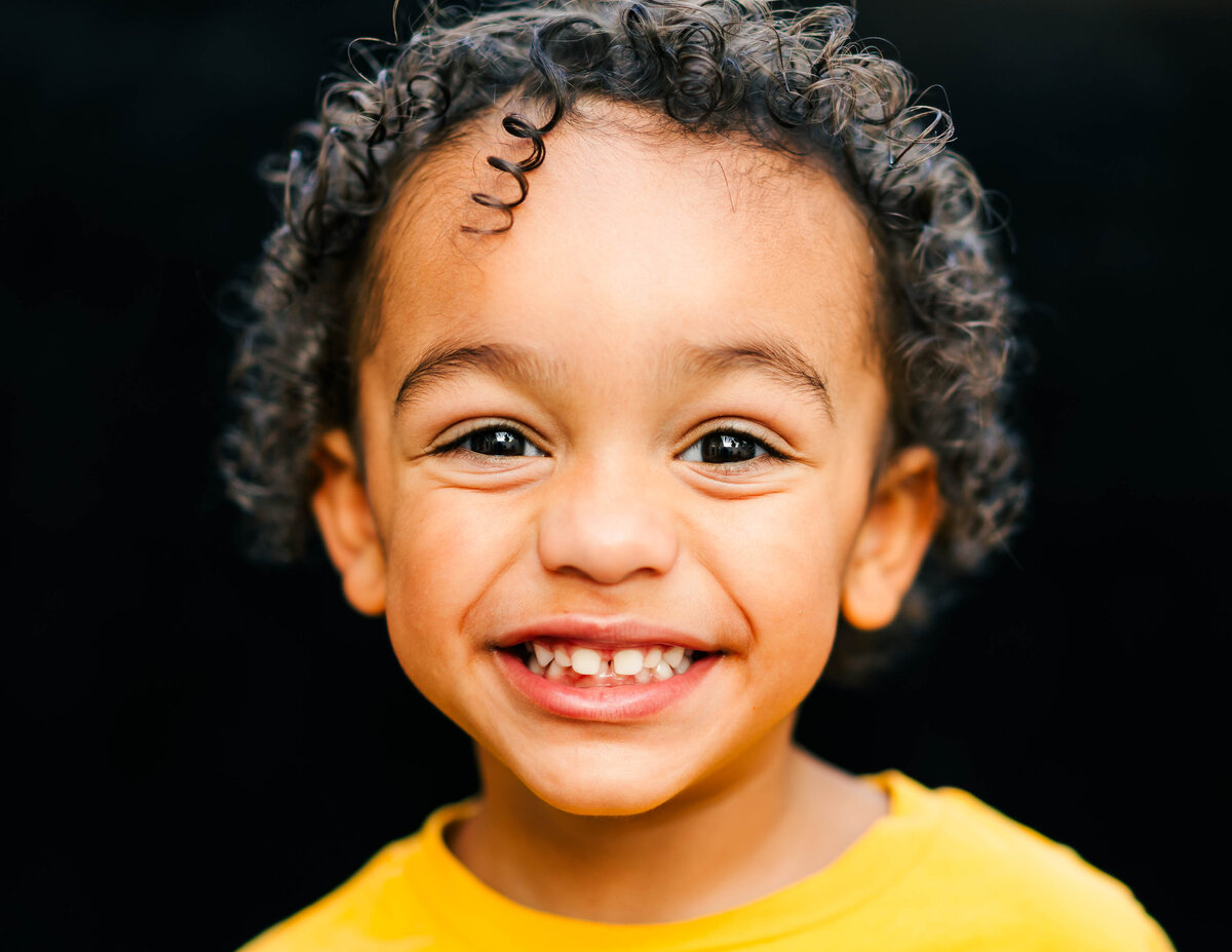 Toddler boy laughing softly, dark background emphasizing expression
