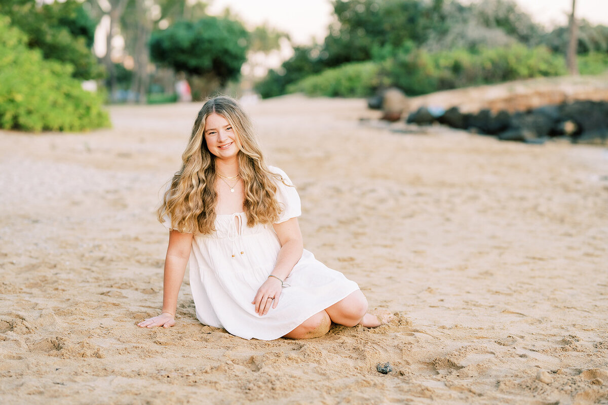 high school senior sitting on the sand and smiling