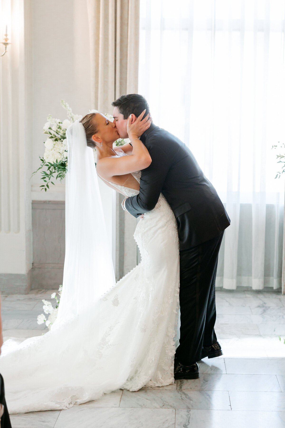 The bride and groom share a dip kiss at the altar, surrounded by lush florals and warm light—captured flawlessly by a Philadelphia wedding photographer.