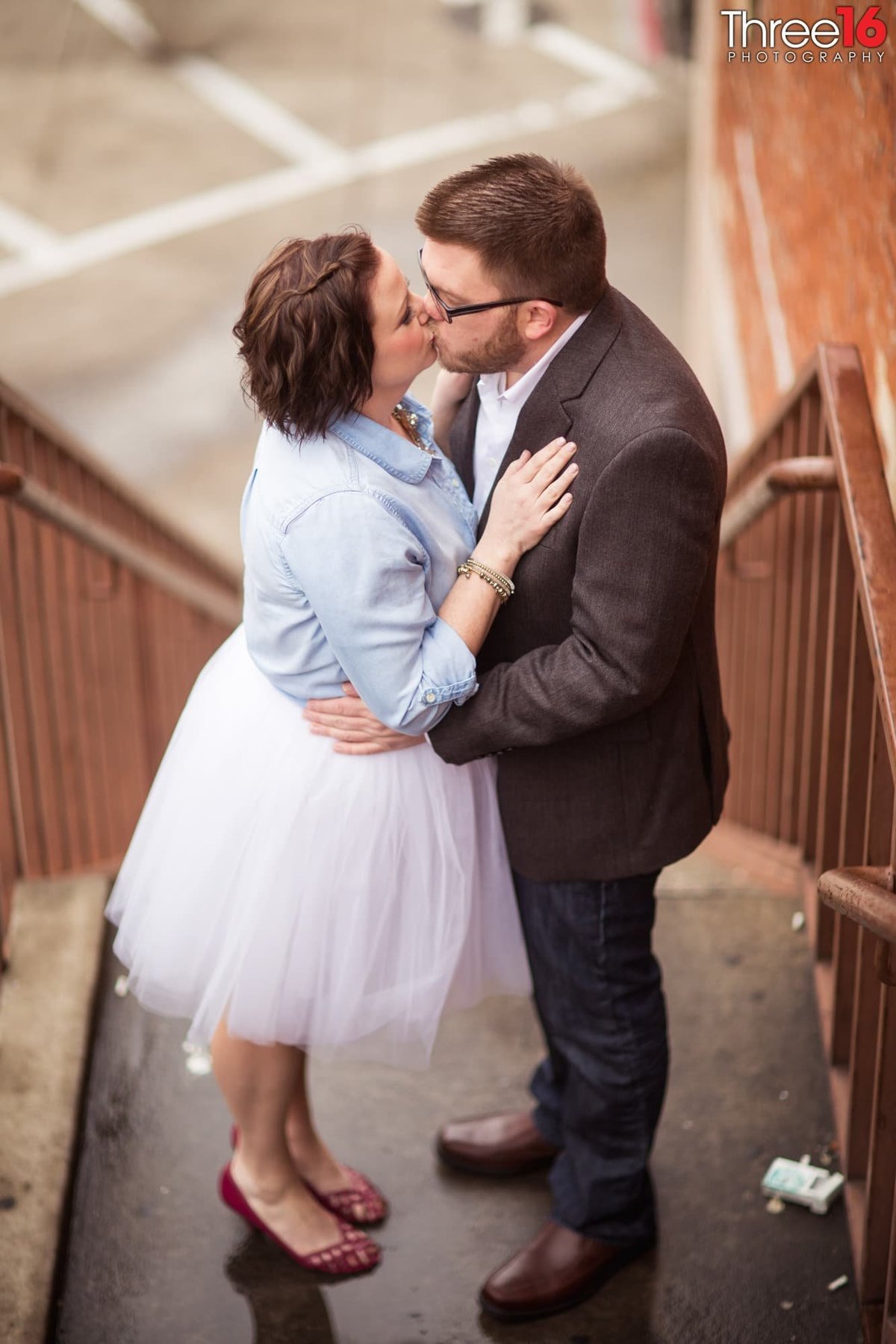 Engaged couple share a kiss on the stairwell of outdoor staircase