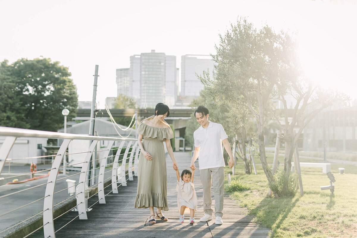 Maternity photo session of family in their green based styling. Mother and father is holding hand of their toddler baby girl while the mother is placing her hand over her pregnant belly.