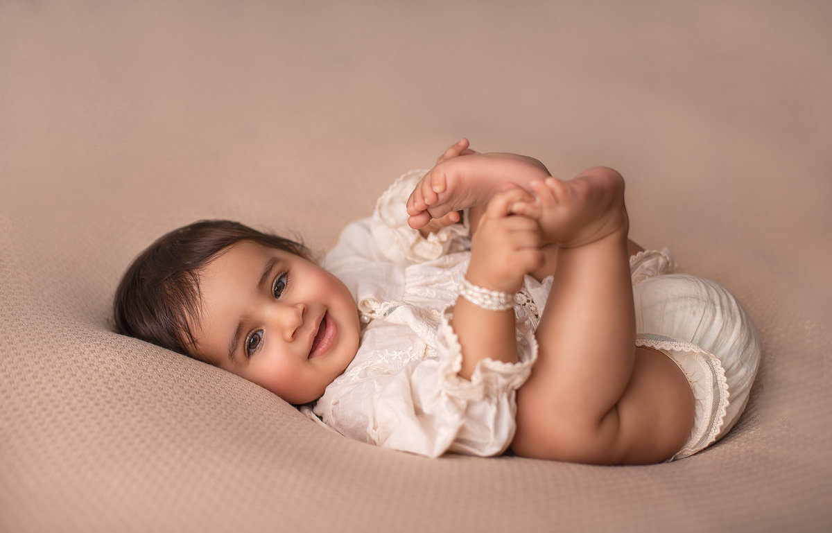 Happy 8-month-old baby lying on back, smiling and holding feet – Milestone photography in Ottawa by Sonia Gourlie