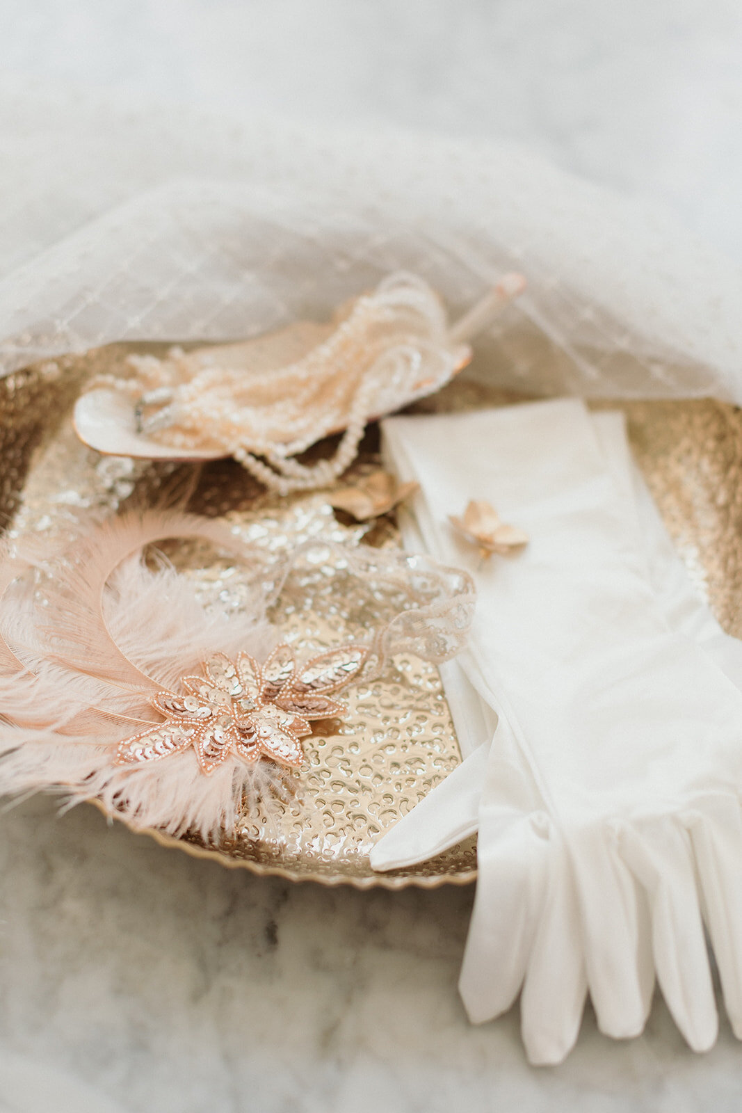 close up photo of dressing items on a gold tray, including white glove, feathered hairpieces and jewelry.