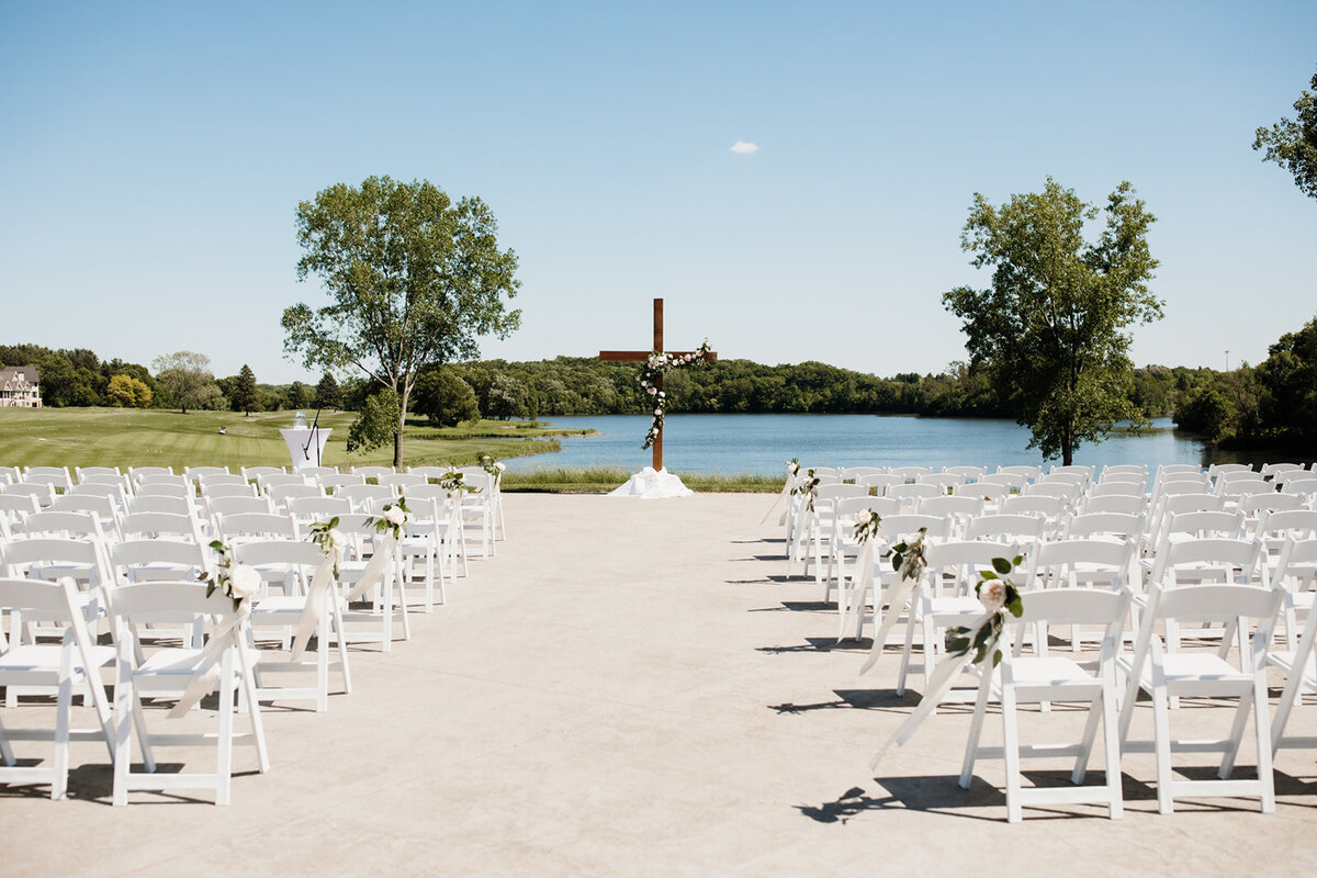 Landscape photo of an outdoor wedding ceremony space with white chairs and a cross at the altar