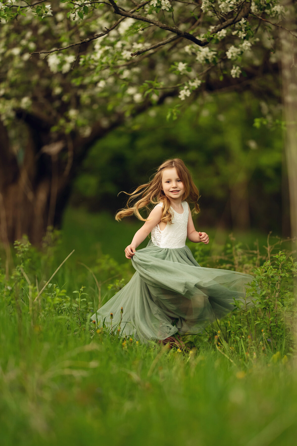 A young girl twirls in a Brookfield, WI meadow with a blossoming tree overhead.