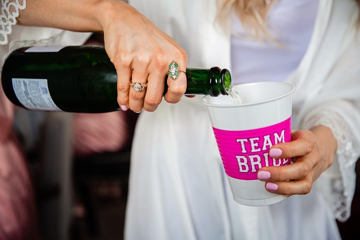 Bride pouring champagne into a Team Bride pink and white solo cup