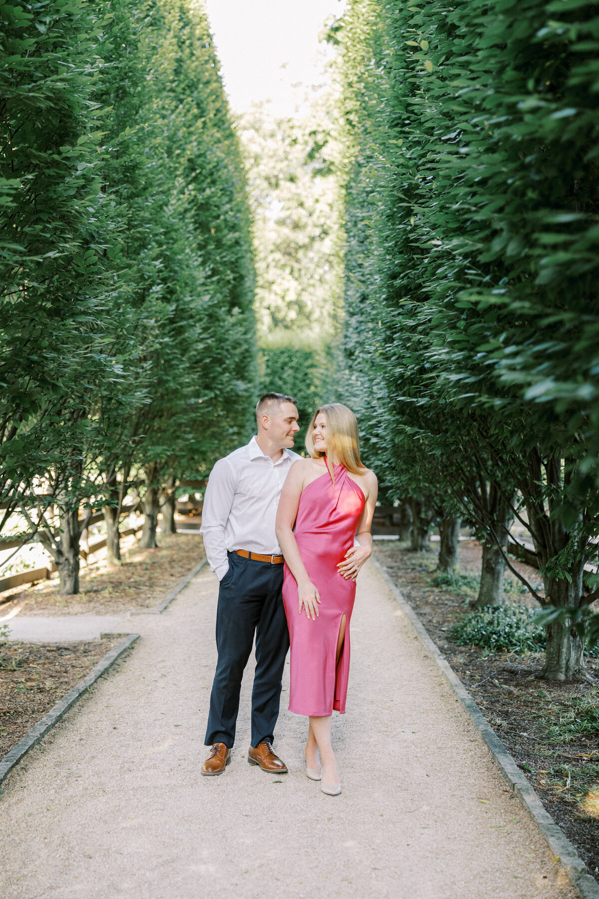 Engaged couple smiling at each other on tree-lined path in Columbus park shot by Philadelphia photographer.