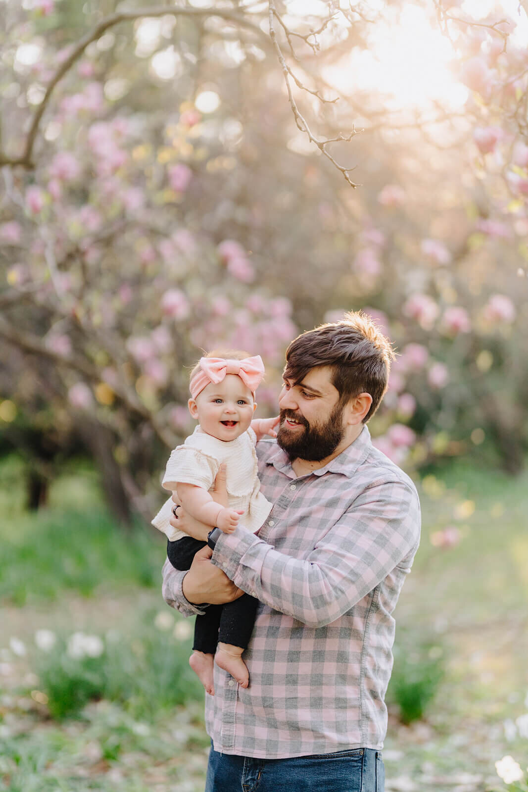 father holding a baby standing in front of a cherry blossom tree