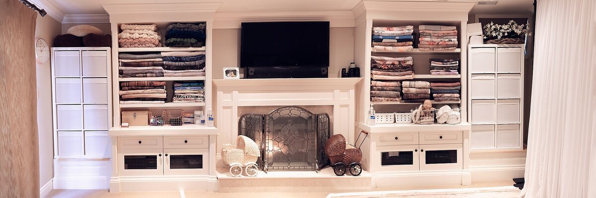 Large built-in storage wall in a newborn photography studio, filled with neatly organized blankets, wraps, props, and backdrops.