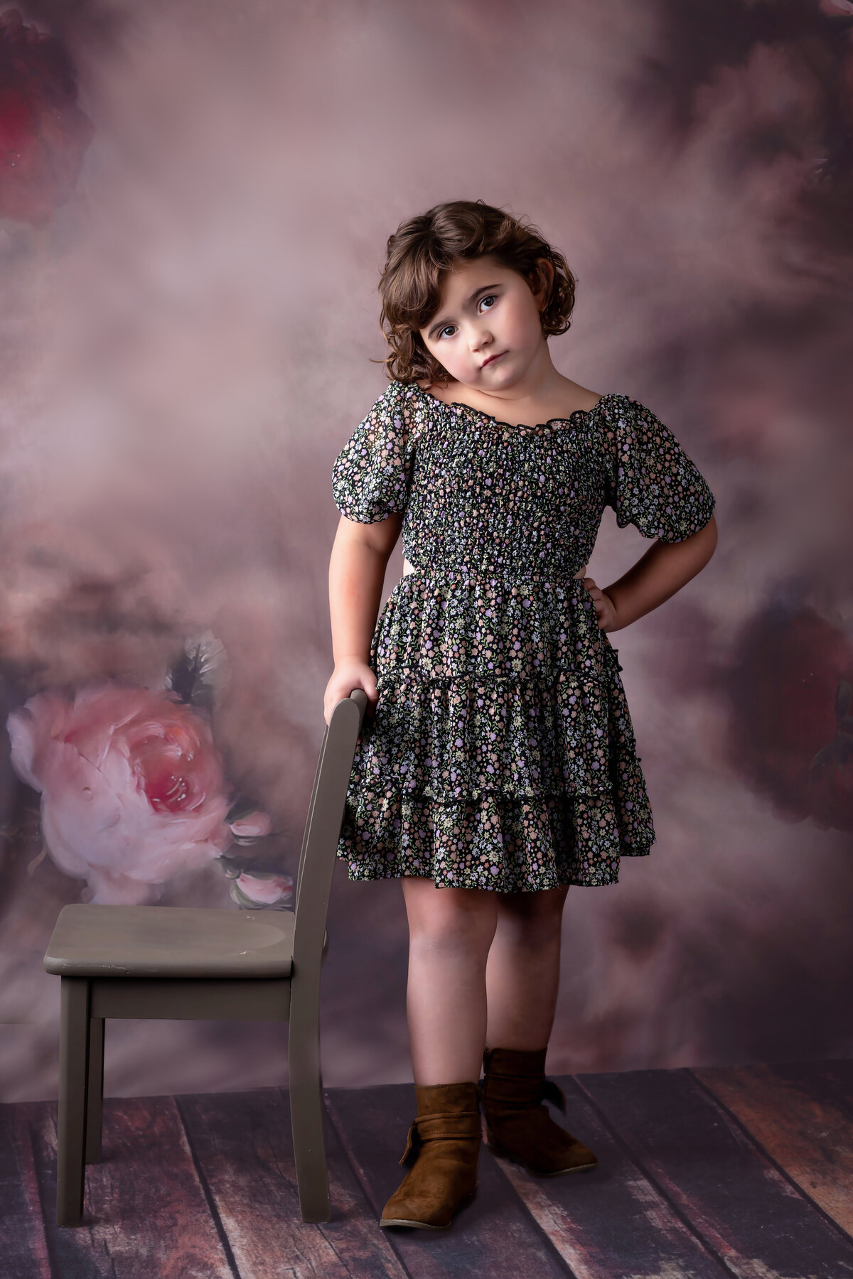 Girl stands looking sassy next to a chair on a floral background in her Iowa Milestone Photos